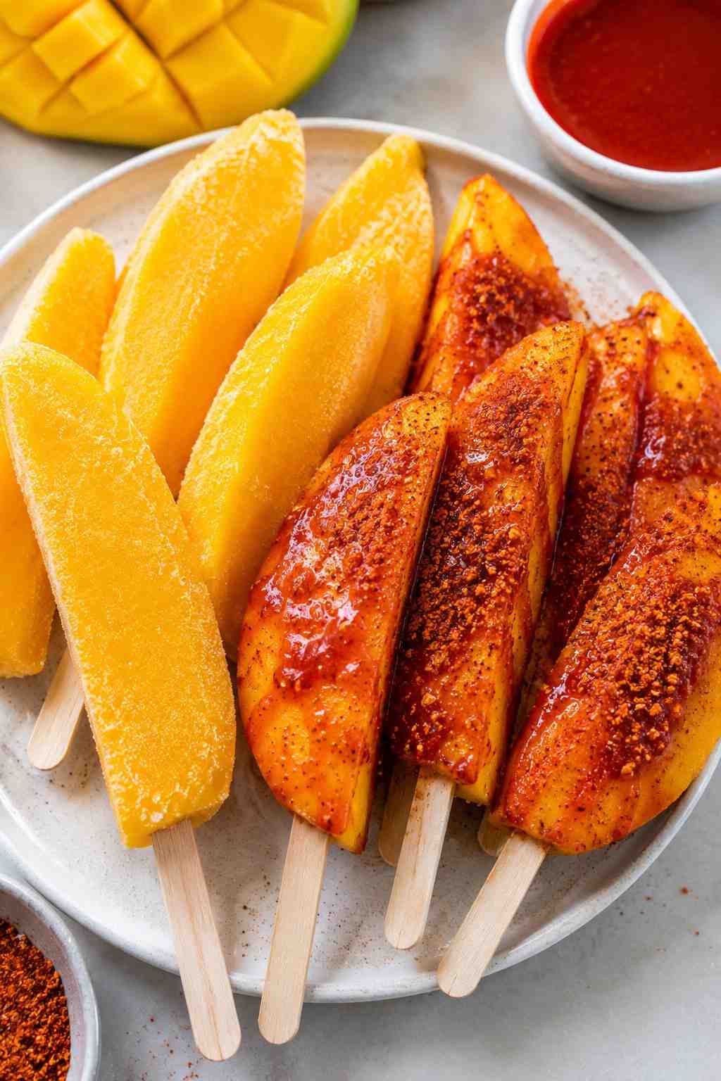 Frozen mango spears on wooden sticks, some plain and some dipped in chamoy and Tajín